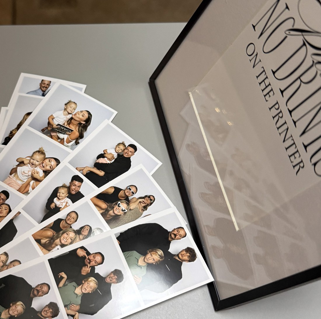 Printed photo strips fanned out on a table beside a framed sign
