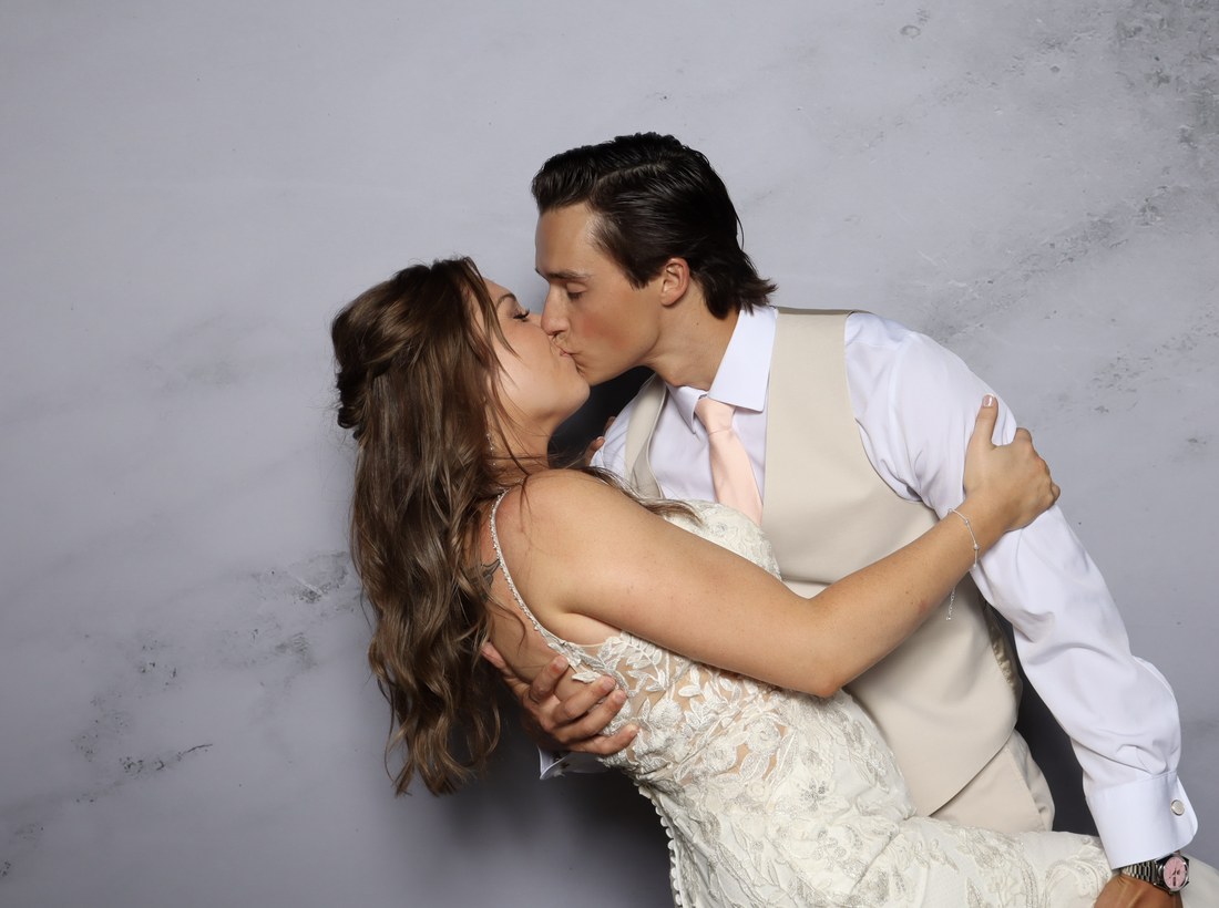 A bride and groom kissing in front of a grey marble backdrop under studio lighting