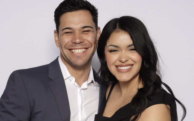 A couple smiling side by side in front of a white backdrop under studio lighting