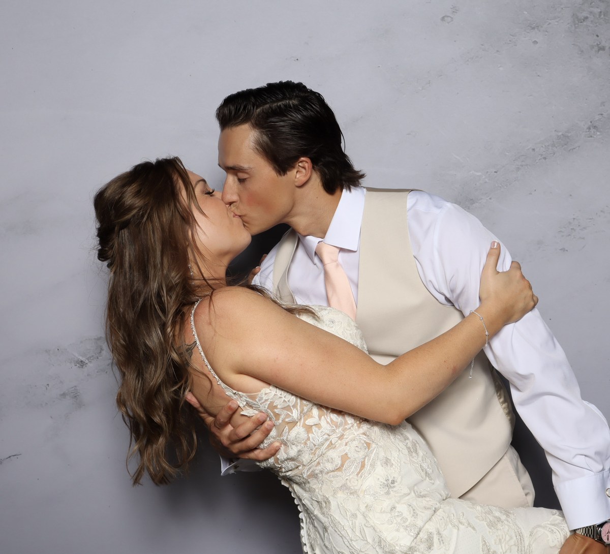 A bride and groom kissing in front of a grey marble backdrop under studio lighting
