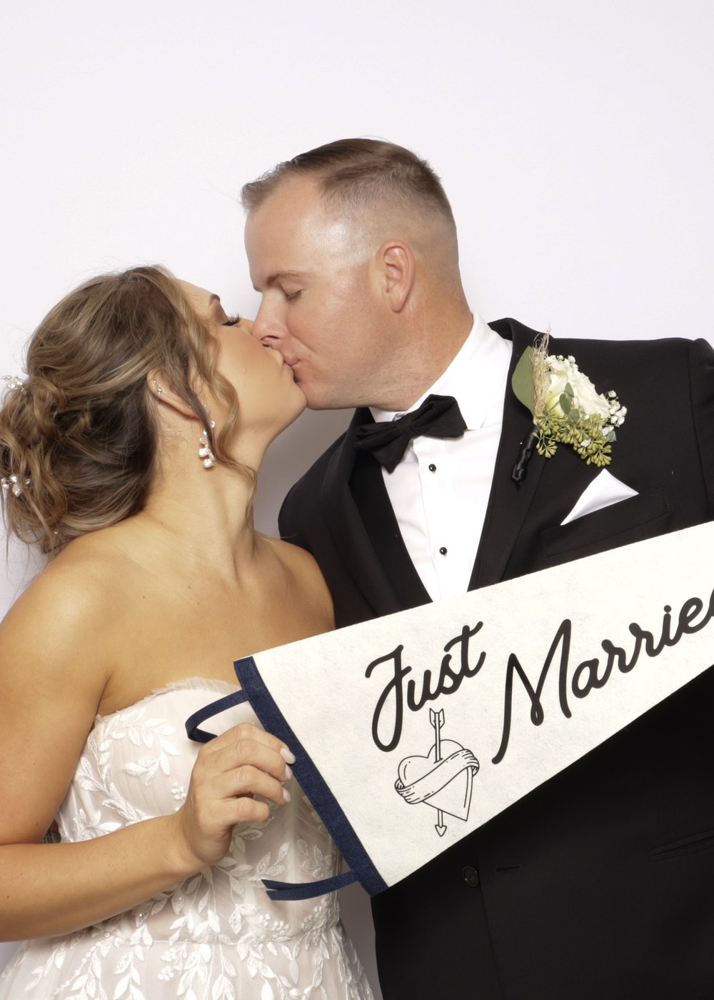 A bride and groom holding a Just Married pennant in front of the booth backdrop